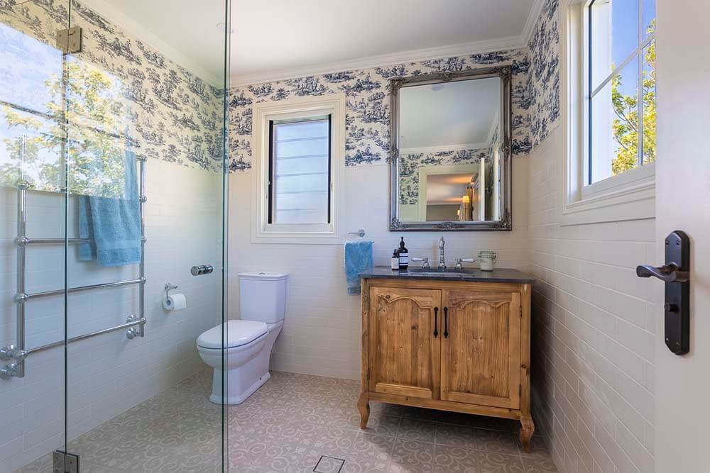 Hartley House French Country Bathroom Classic bathroom at Hartley House with blue toile wallpaper, timber vanity, chrome tapware, patterned floor tiles and traditional door hardware.