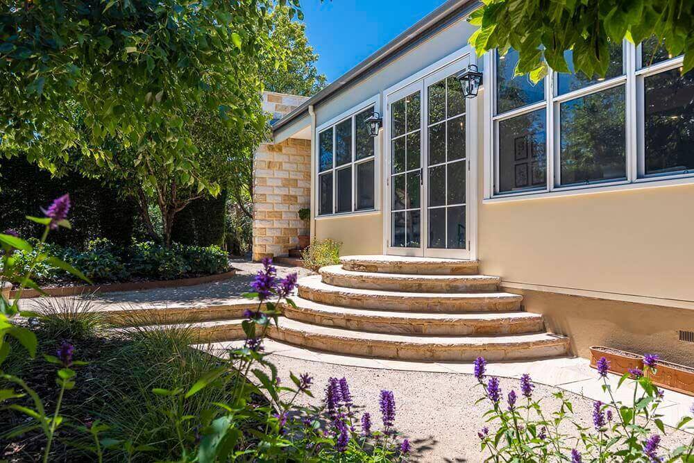 Hartley House Exterior French-country sandstone exterior at Hartley House with French doors, garden steps, traditional wall lanterns and landscaped gardens.